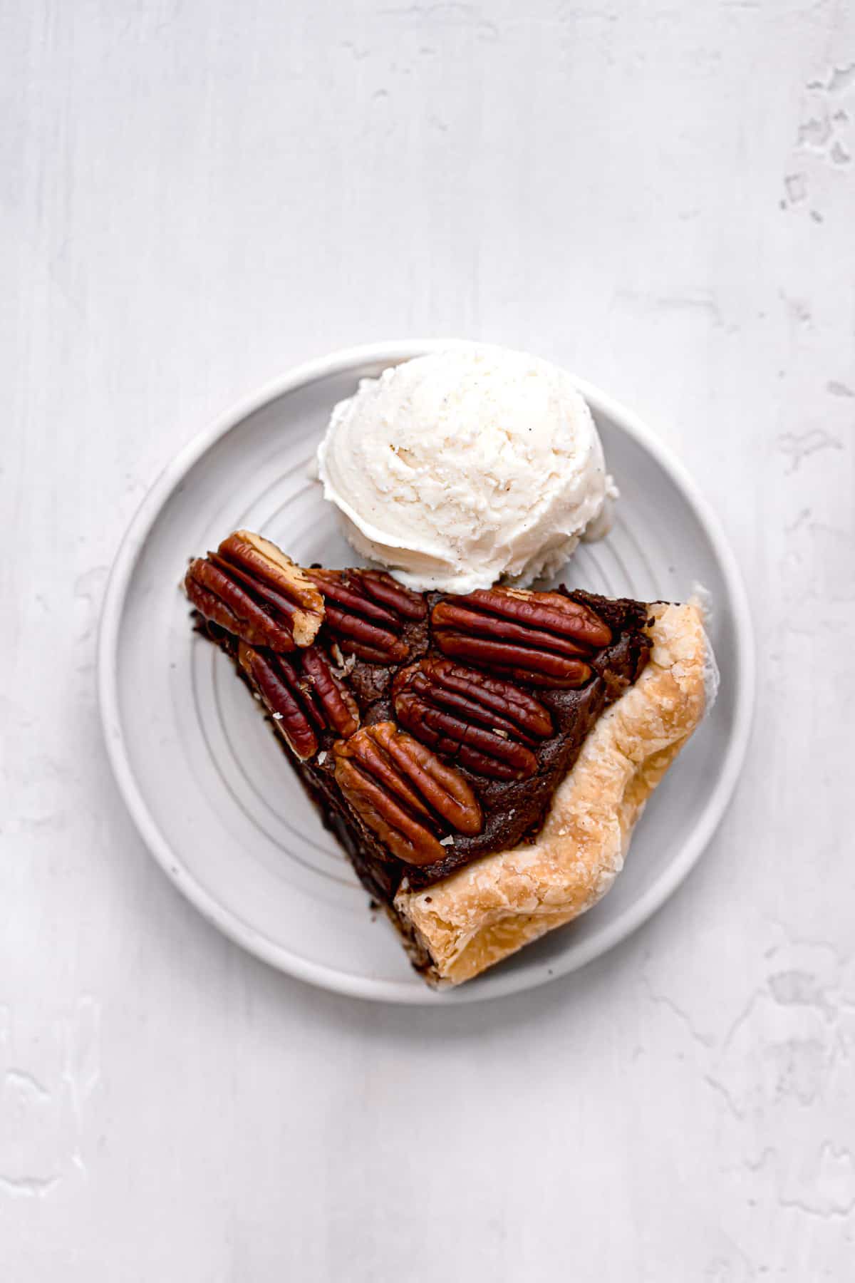 slice of pecan brownie pie on white plate with scoop of vanilla ice cream.