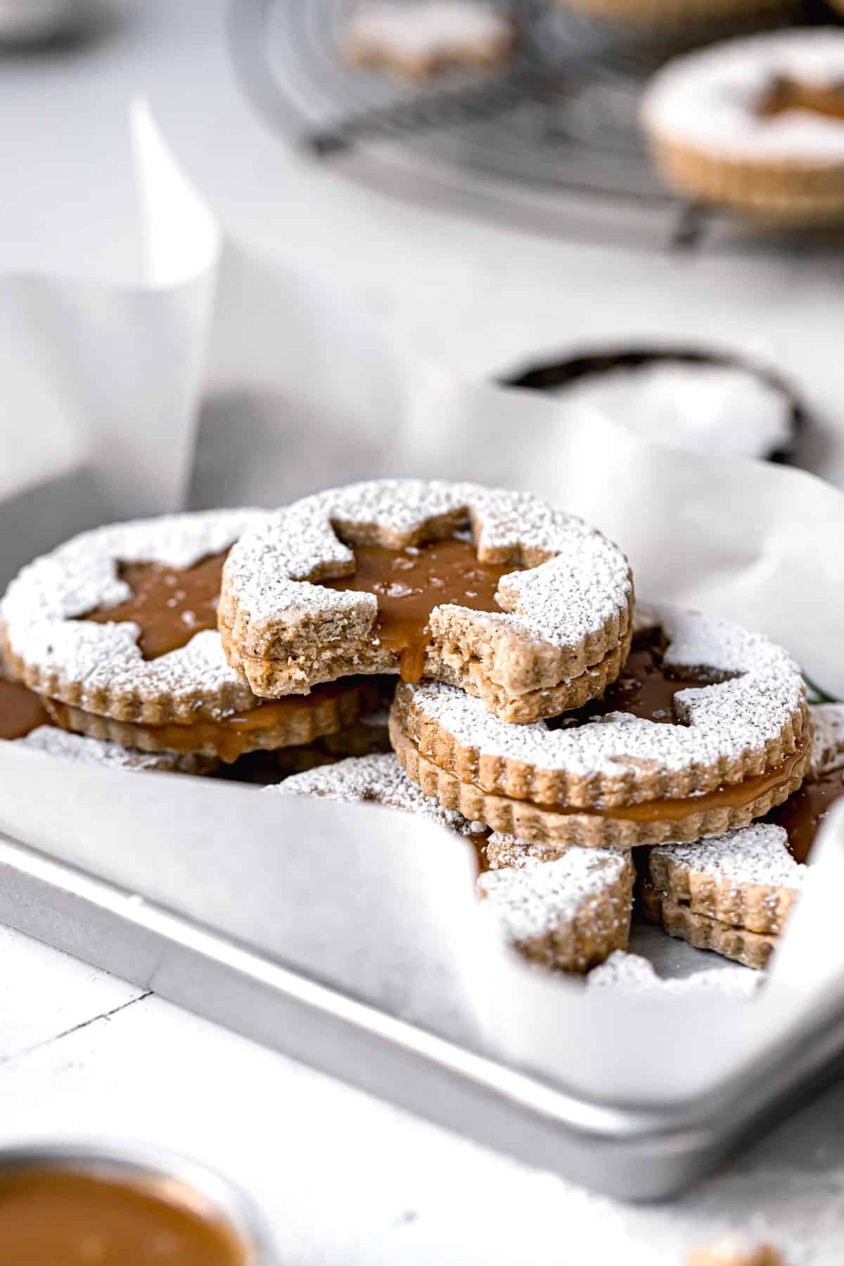 caramel linzer cookies stacked in parchment lined baking sheet.