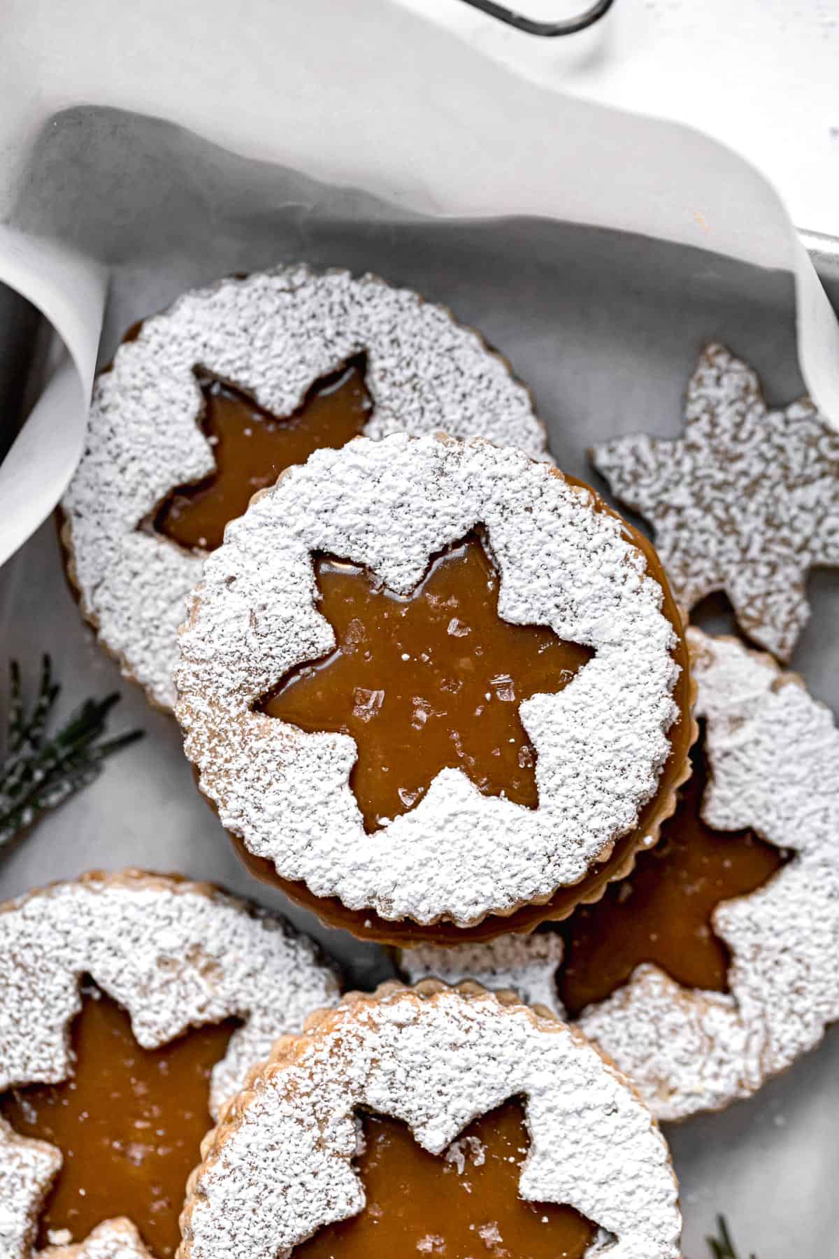 salted caramel christmas linzer cookies piled in small baking sheet.
