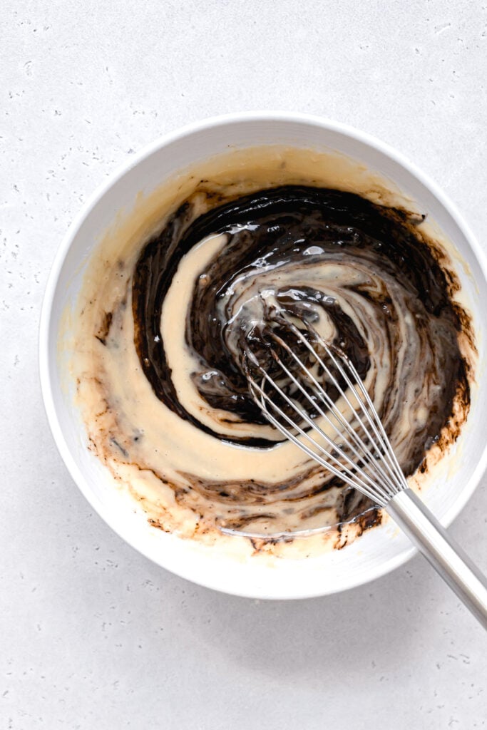 melted chocolate being mixed into donut batter in white bowl