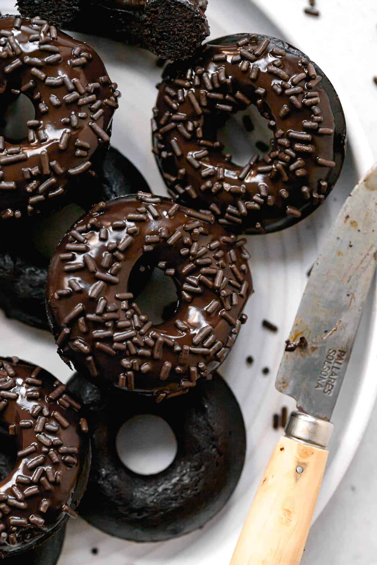 chocolate covered donuts on white plate with small knife.