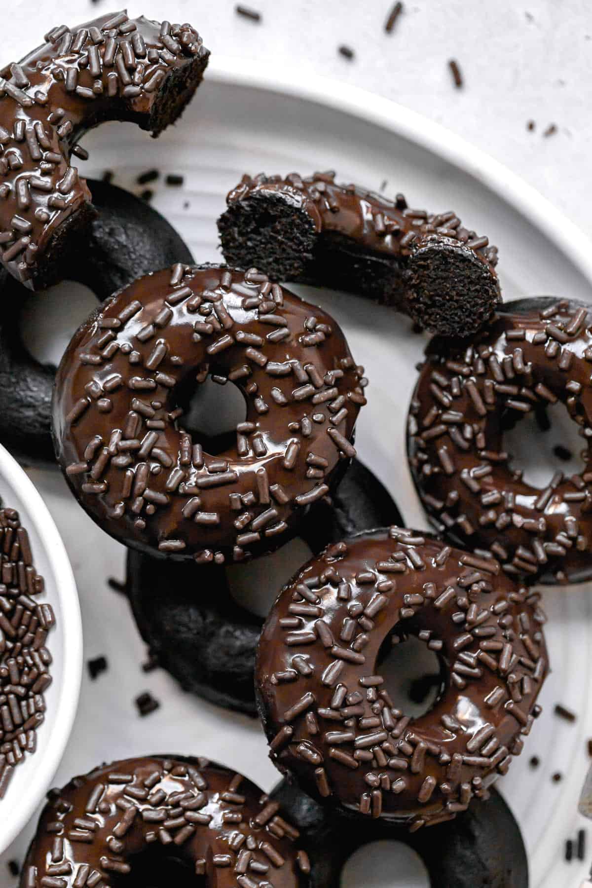 double chocolate glazed donuts with sprinkles layered on white plate.