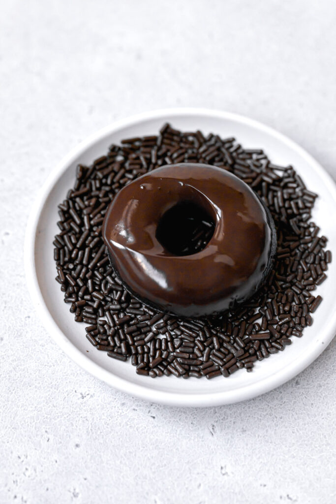 chocolate donut dipped in glaze and sitting on a white plate full of sprinkles 