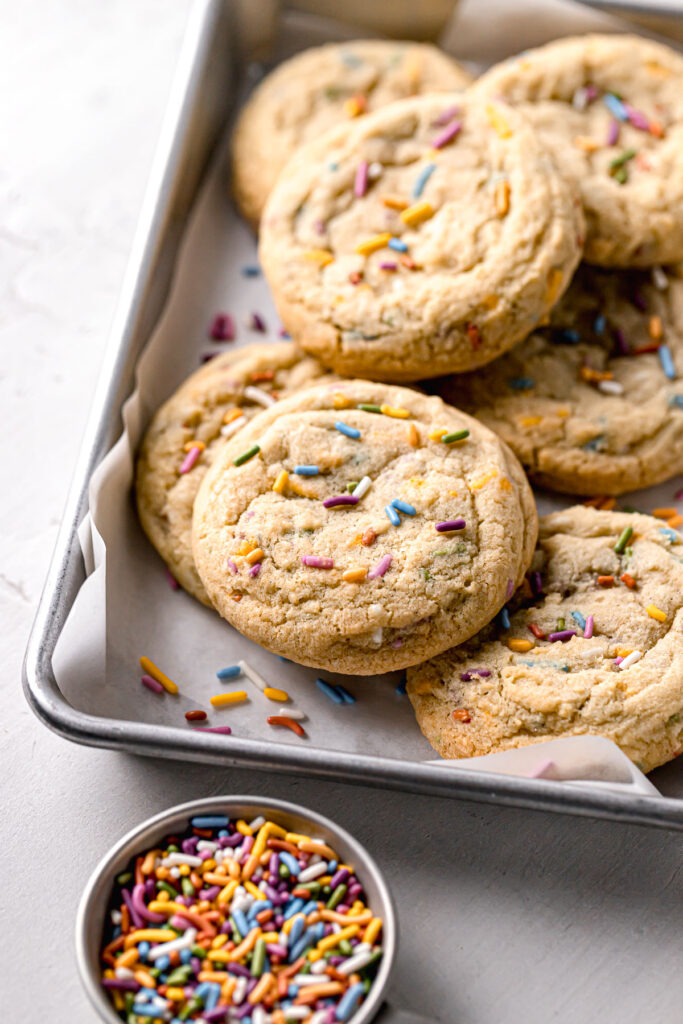 funfetti cookies piled in parchment lined baking sheet