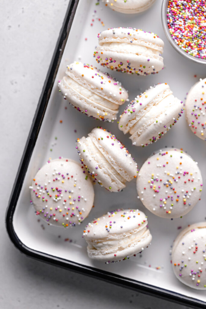 birthday cake macarons with rainbow sprinkles and whipped cream cheese frosting arranged in white tray