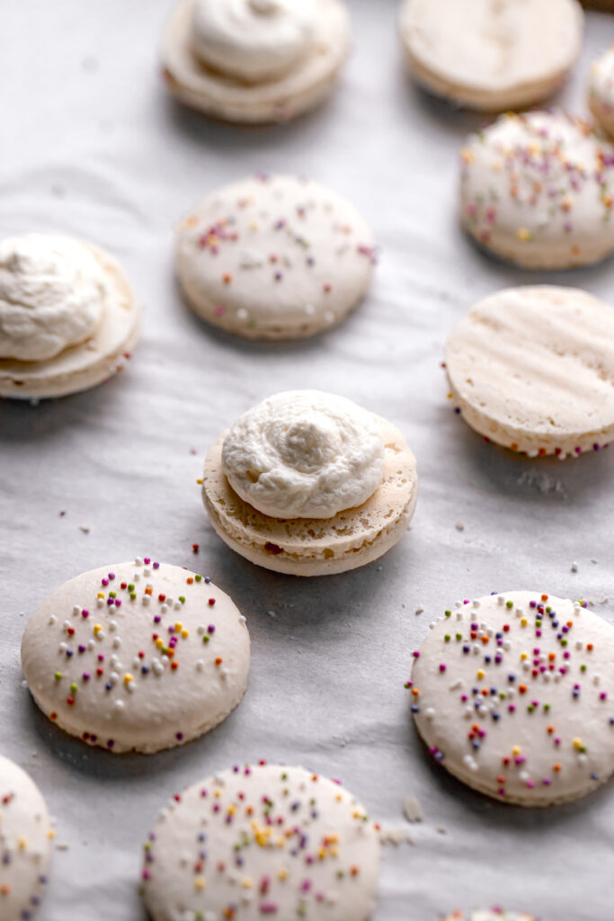 whipped cream cheese frosting piped onto bottom birthday cake macaron shells