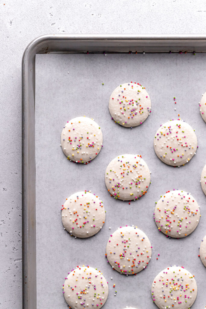 vanilla macaron batter piped onto parchment lined baking sheet and topped with rainbow sprinkles