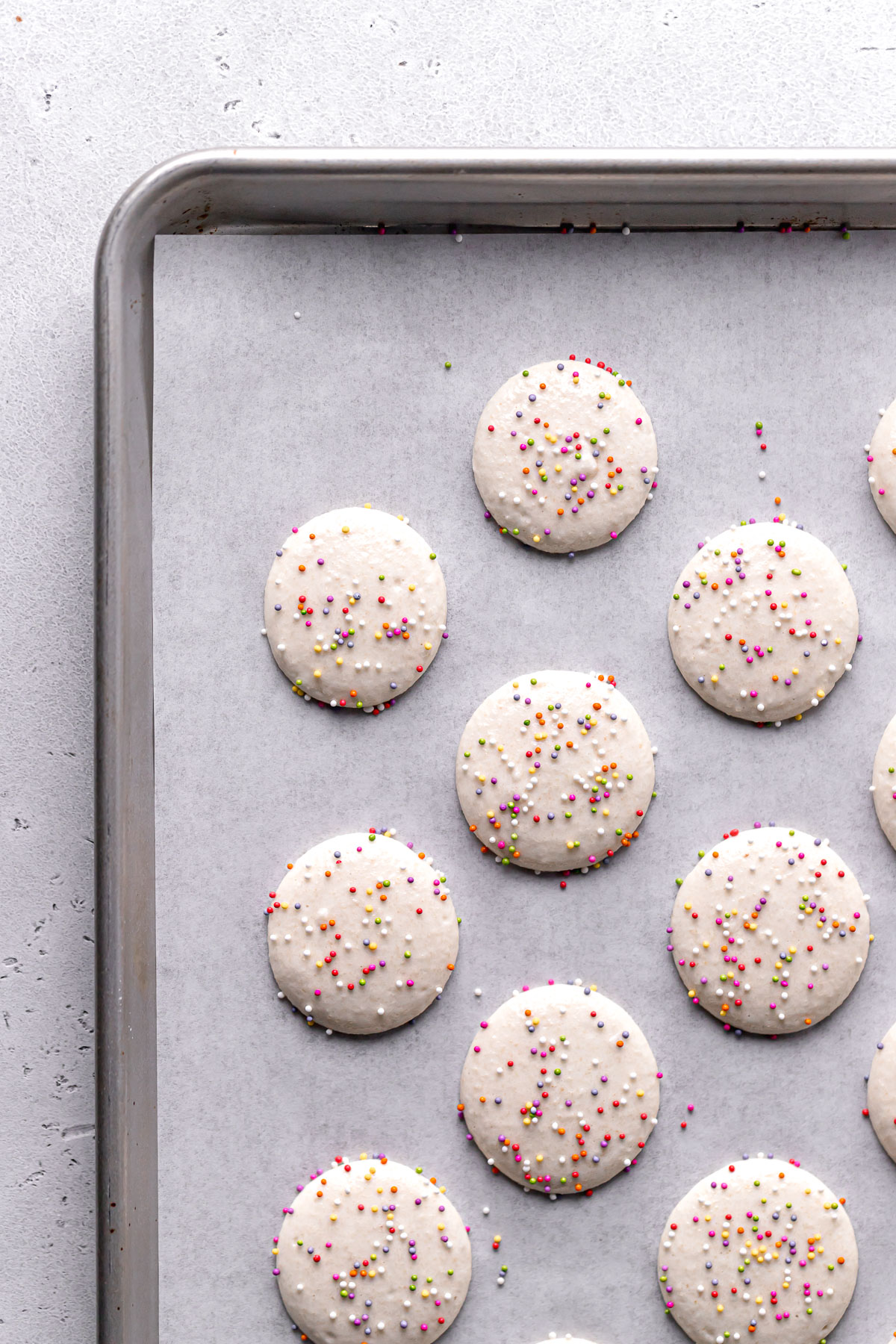 vanilla macaron batter piped onto parchment lined baking sheet and topped with rainbow sprinkles.