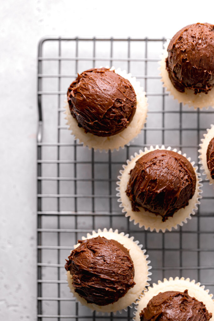 dark chocolate frosting scooped onto vanilla cupcakes