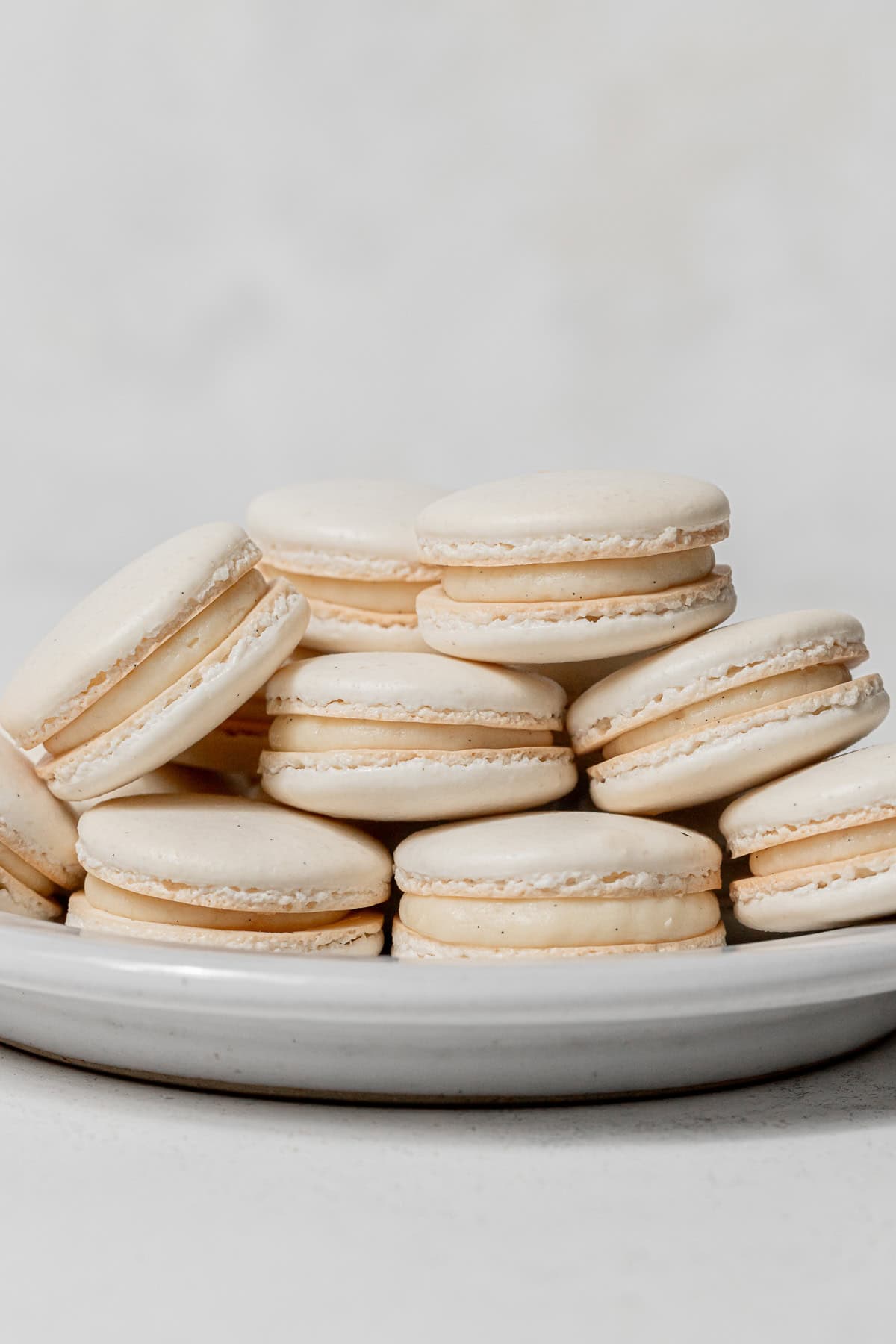 vanilla macarons piled on white plate.