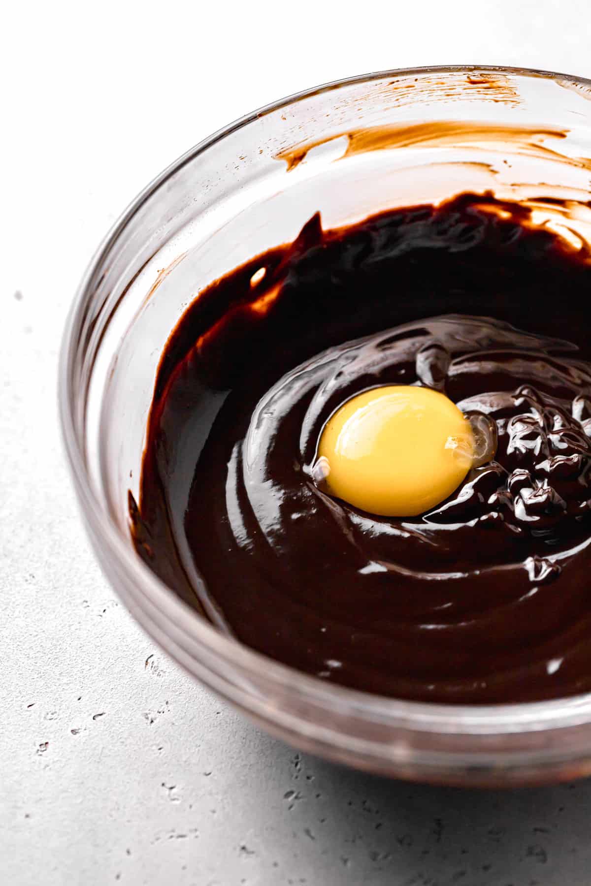 egg yolk added to chocolate mixture in glass bowl.