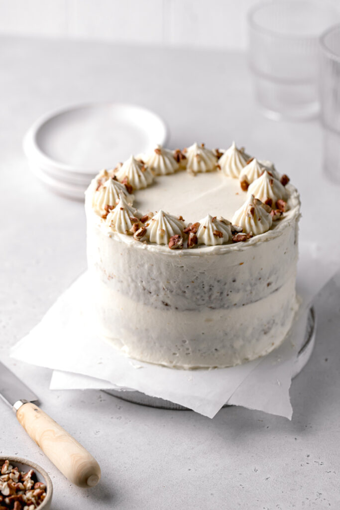 small carrot cake with cream cheese frosting topped with pecans on white wooden board