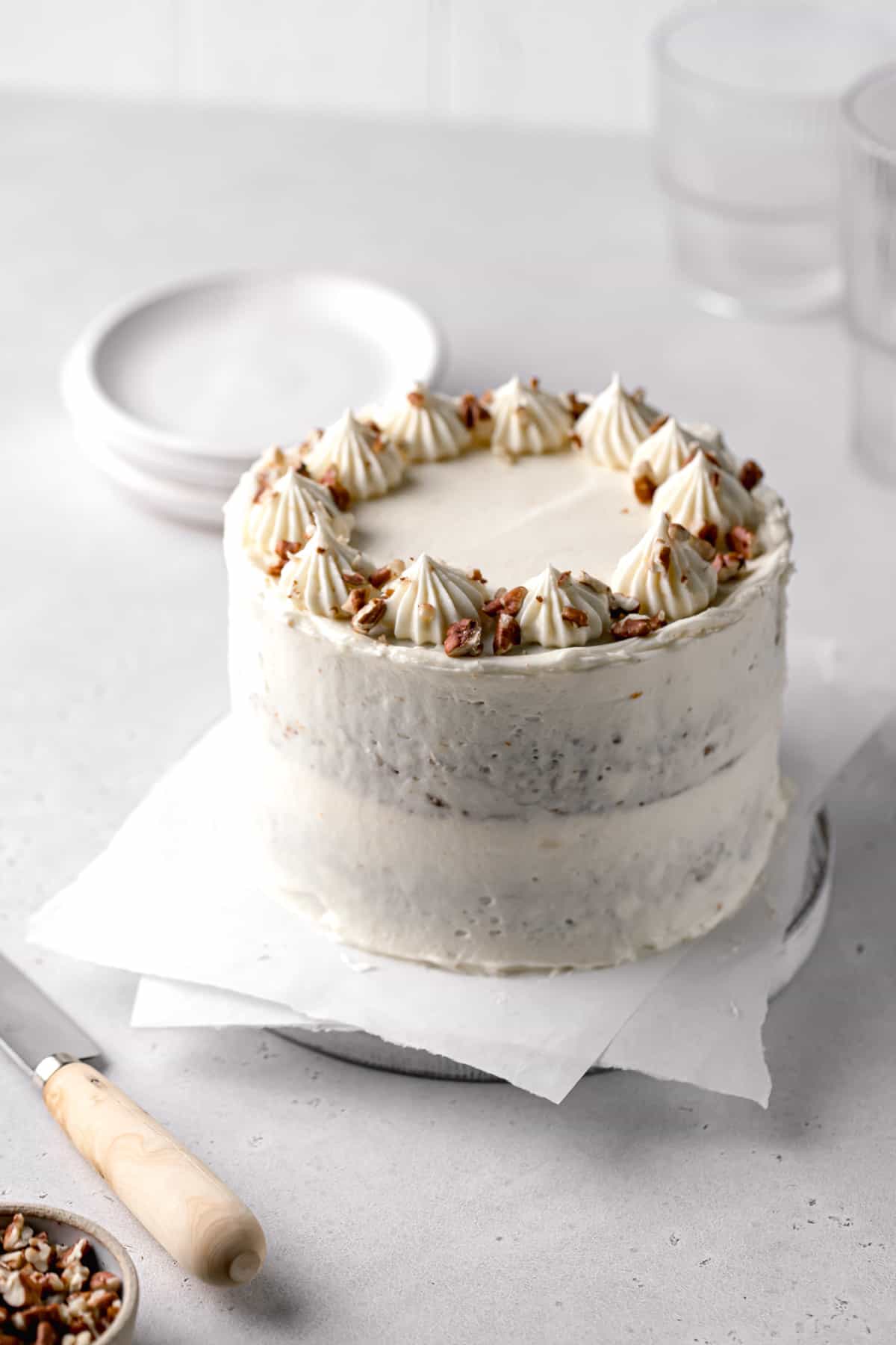 small carrot cake with cream cheese frosting topped with pecans on white wooden board.
