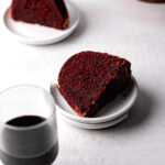 slice of red velvet bundt cake on plate with glass of wine in foreground
