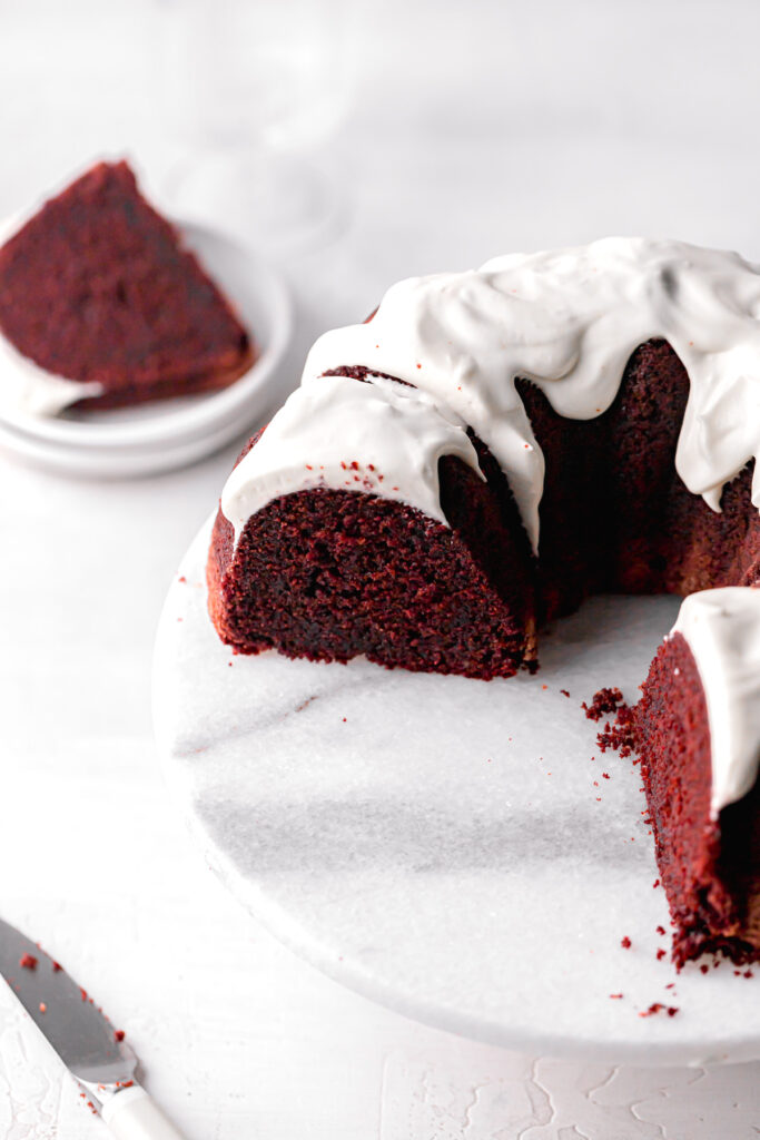 red velvet bundt cake with cream cheese frosting on marble cake stand and cut to reveal interior 