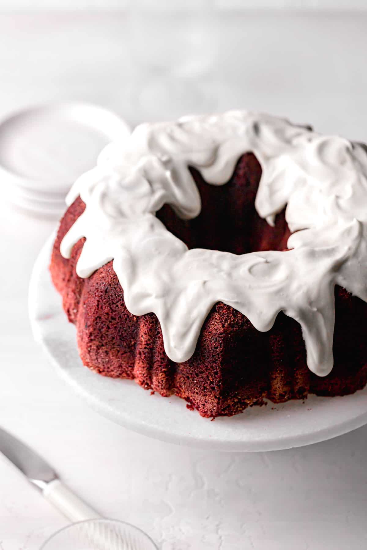 red velvet bundt cake with cream cheese frosting on marble cake stand.