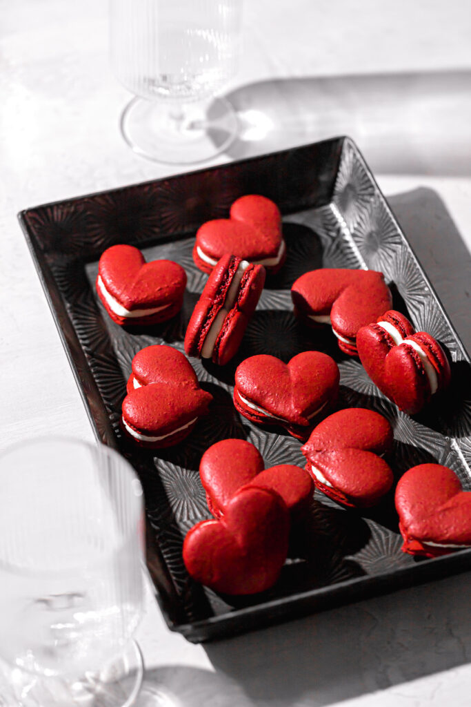 red velvet macarons shaped as hearts and filled with mascarpone frosting