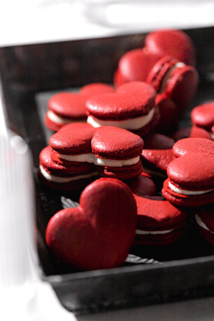 red velvet macarons piled in tray with wine glass in foreground