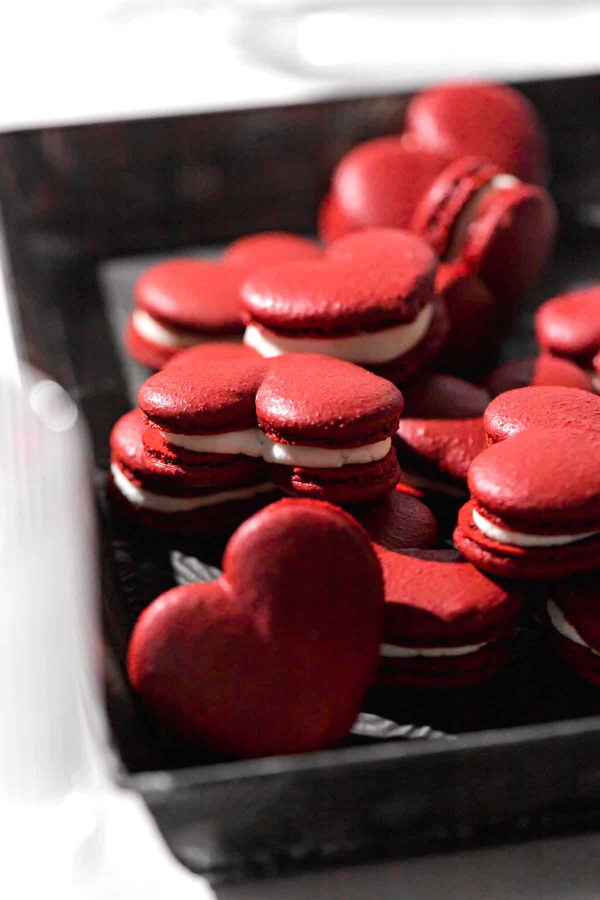 red velvet macarons piled in tray with wine glass in foreground.