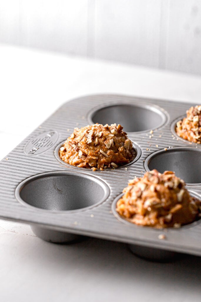 batter piled high in each muffin cavity and topped with pecans