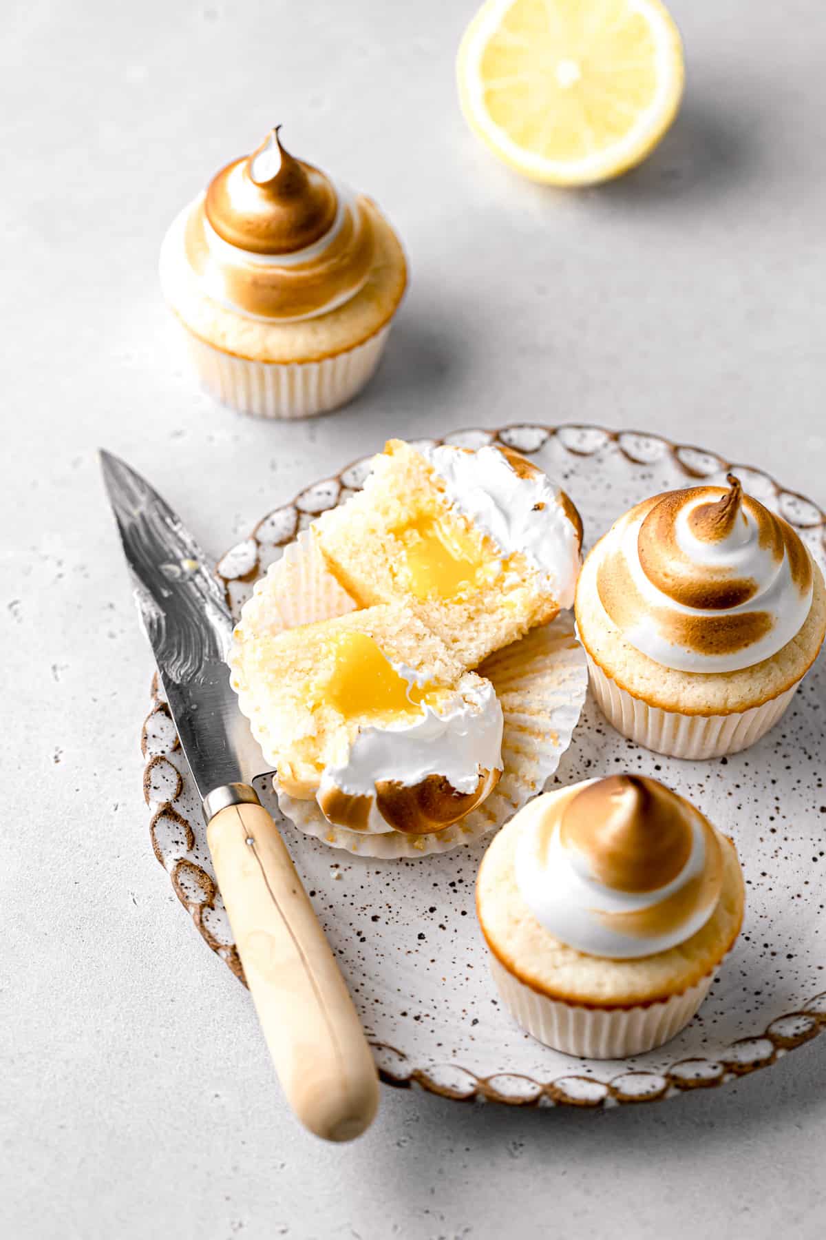 lemon meringue cupcakes on plate with one cut in half.