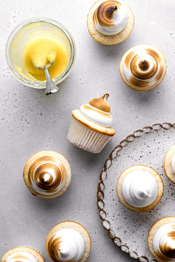 lemon meringue cupcakes on plate and surrounding it with jar of lemon curd