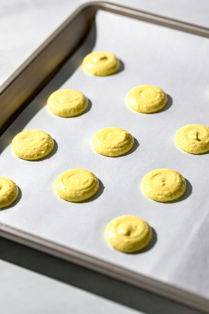yellow macaron batter piped onto parchment lined baking sheet