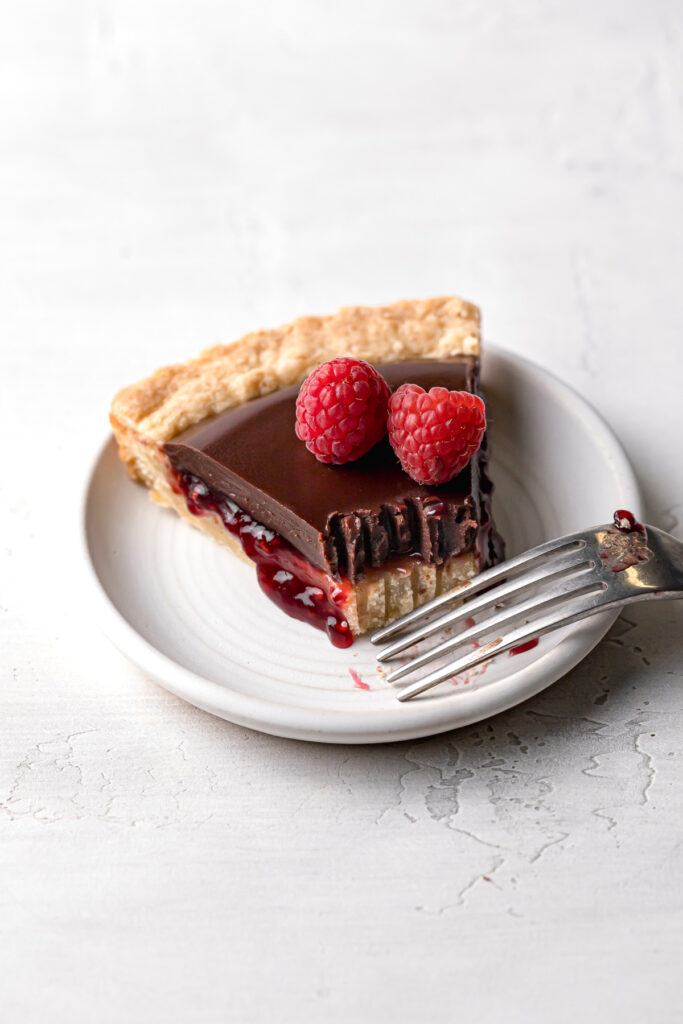 Slice of chocolate raspberry tart on small white plate with fork