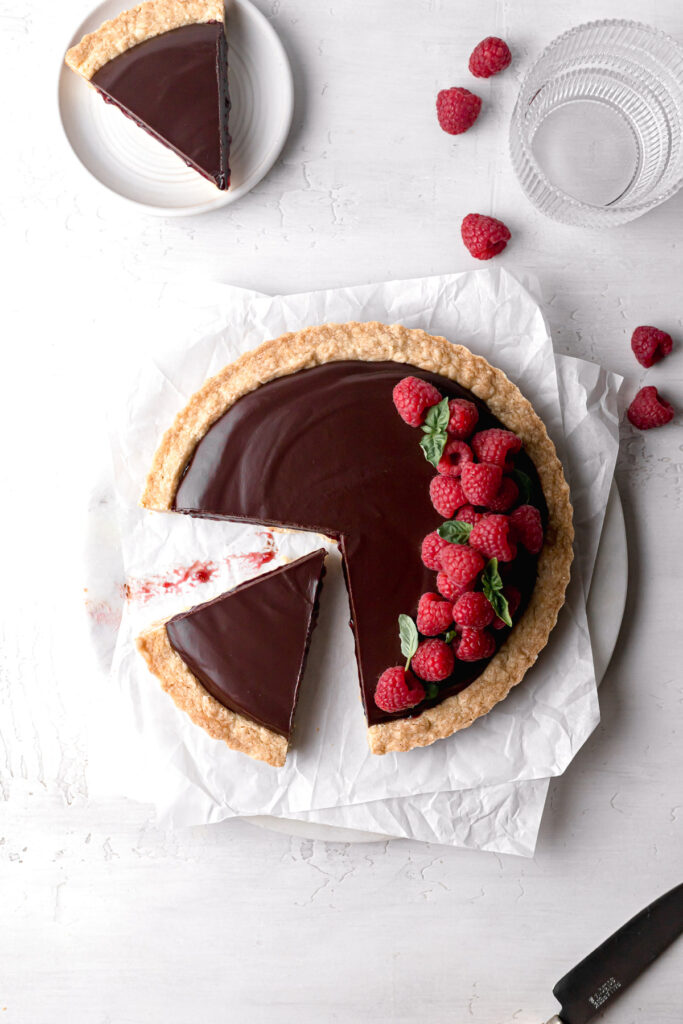 chocolate raspberry tart on parchment paper with fresh raspberries on top