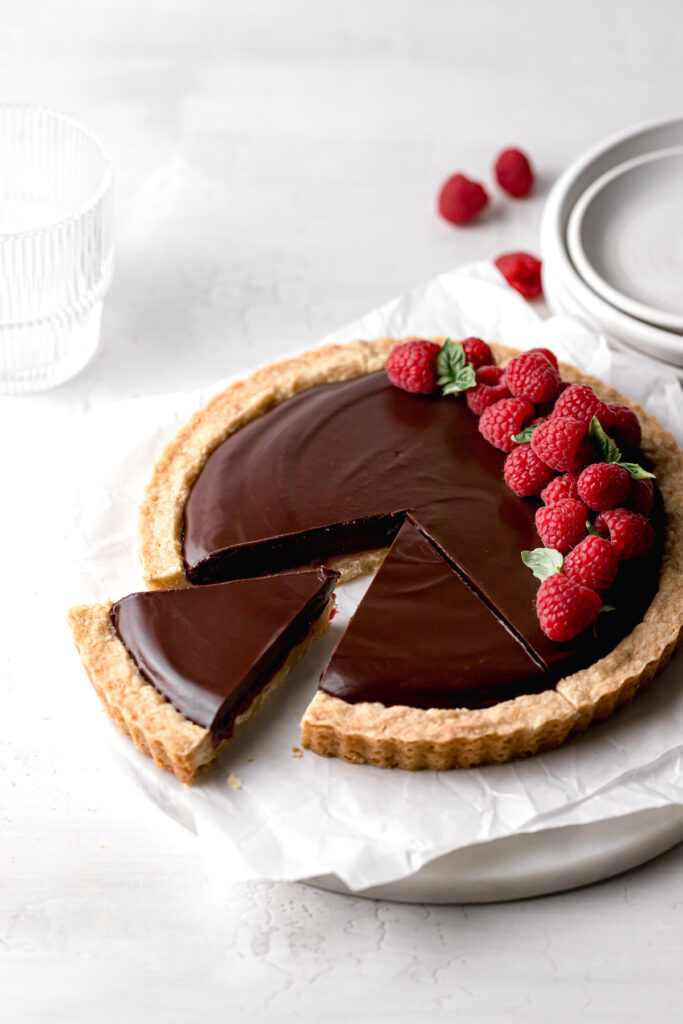 slices cut out of chocolate raspberry tart with fresh raspberries on top