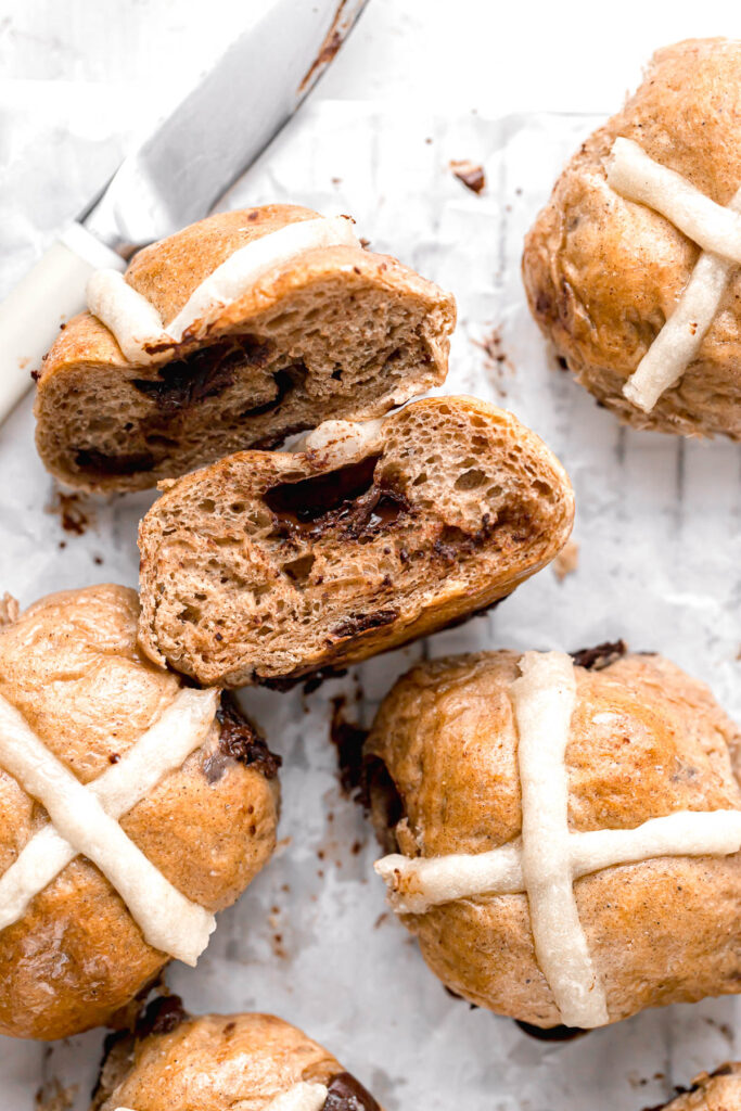 chocolate chip hot cross buns on parchment paper with one cut in half