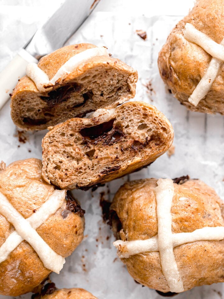 chocolate chip hot cross buns on parchment paper with one cut in half