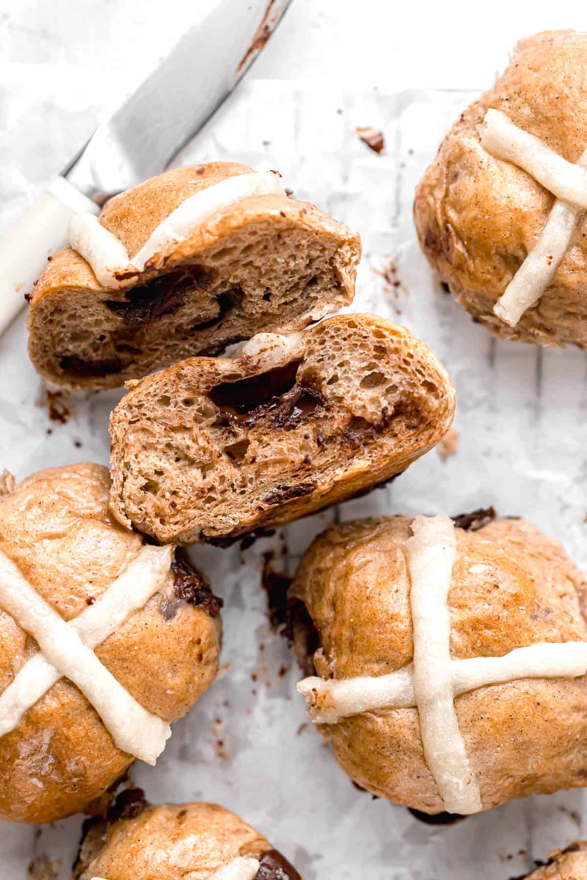chocolate chip hot cross buns on parchment paper with one cut in half.