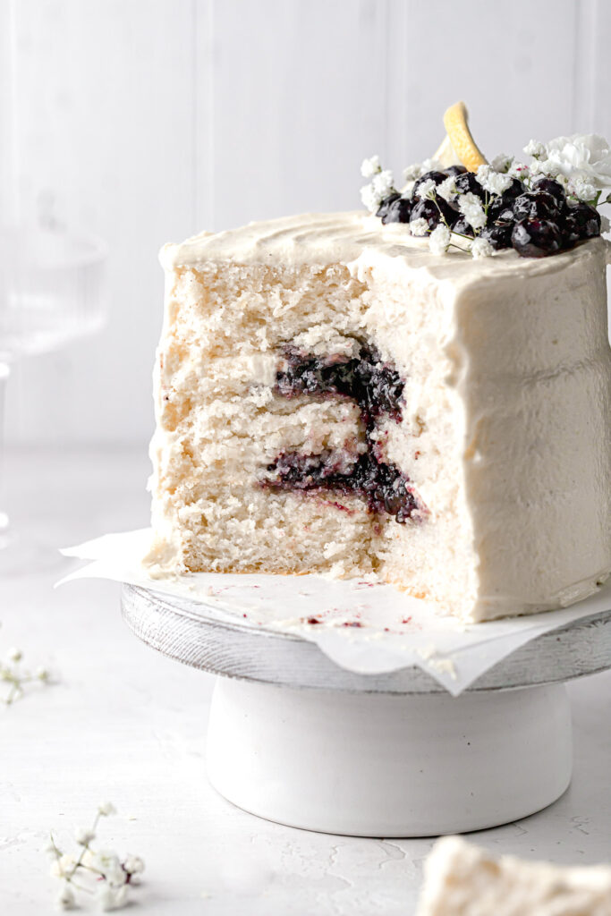 lemon blueberry jam cake on cake stand with several slices taken out to reveal inside