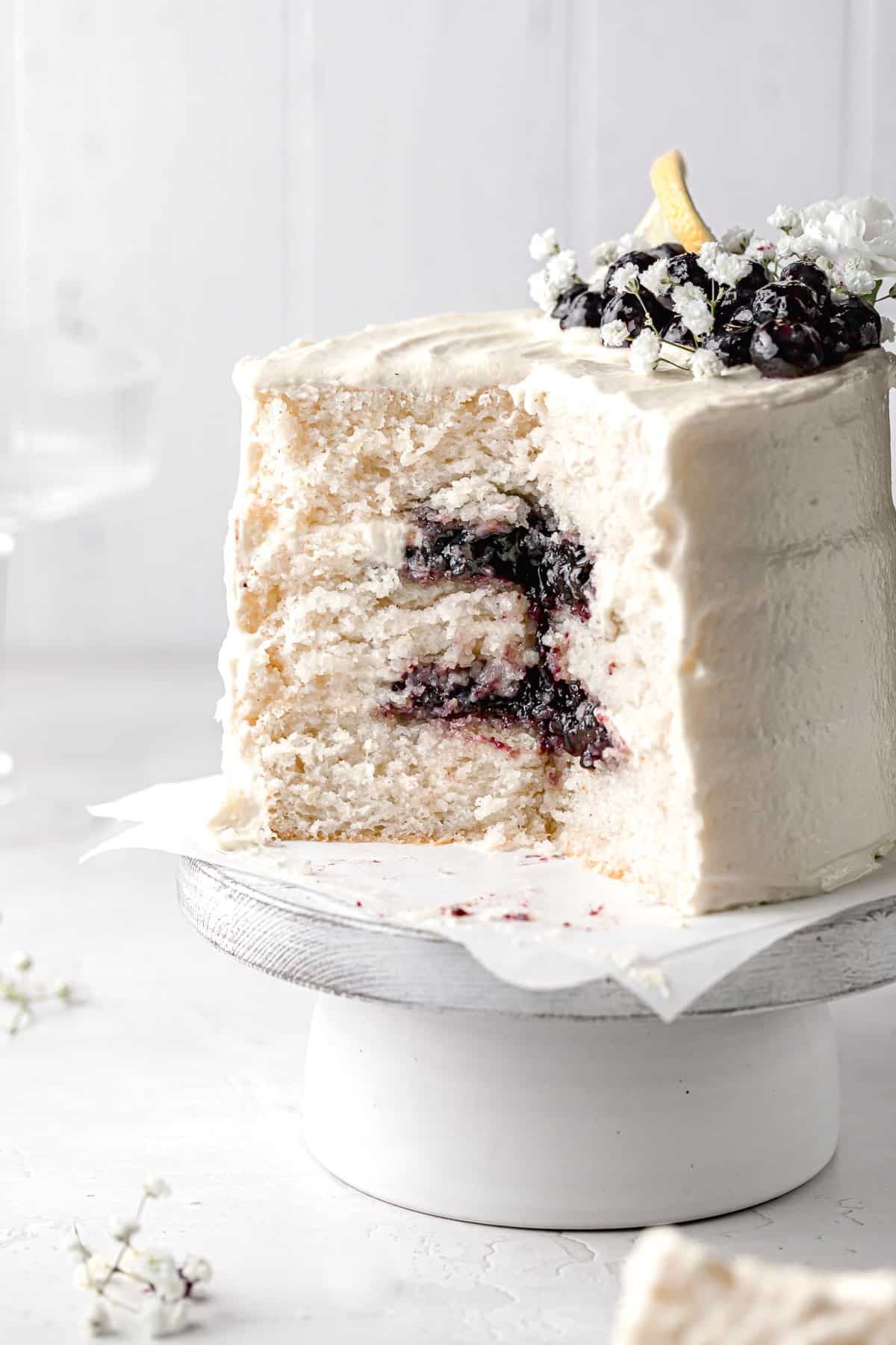 lemon blueberry jam cake on cake stand with several slices taken out to reveal inside.