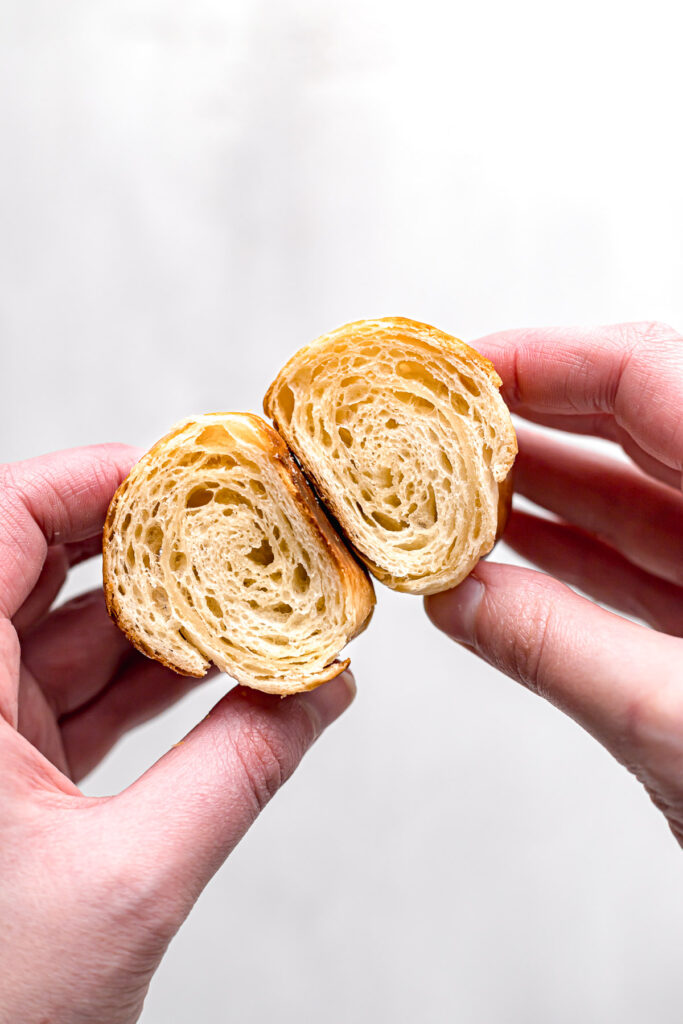 mini croissant cut in half to show inside texture held in two hands