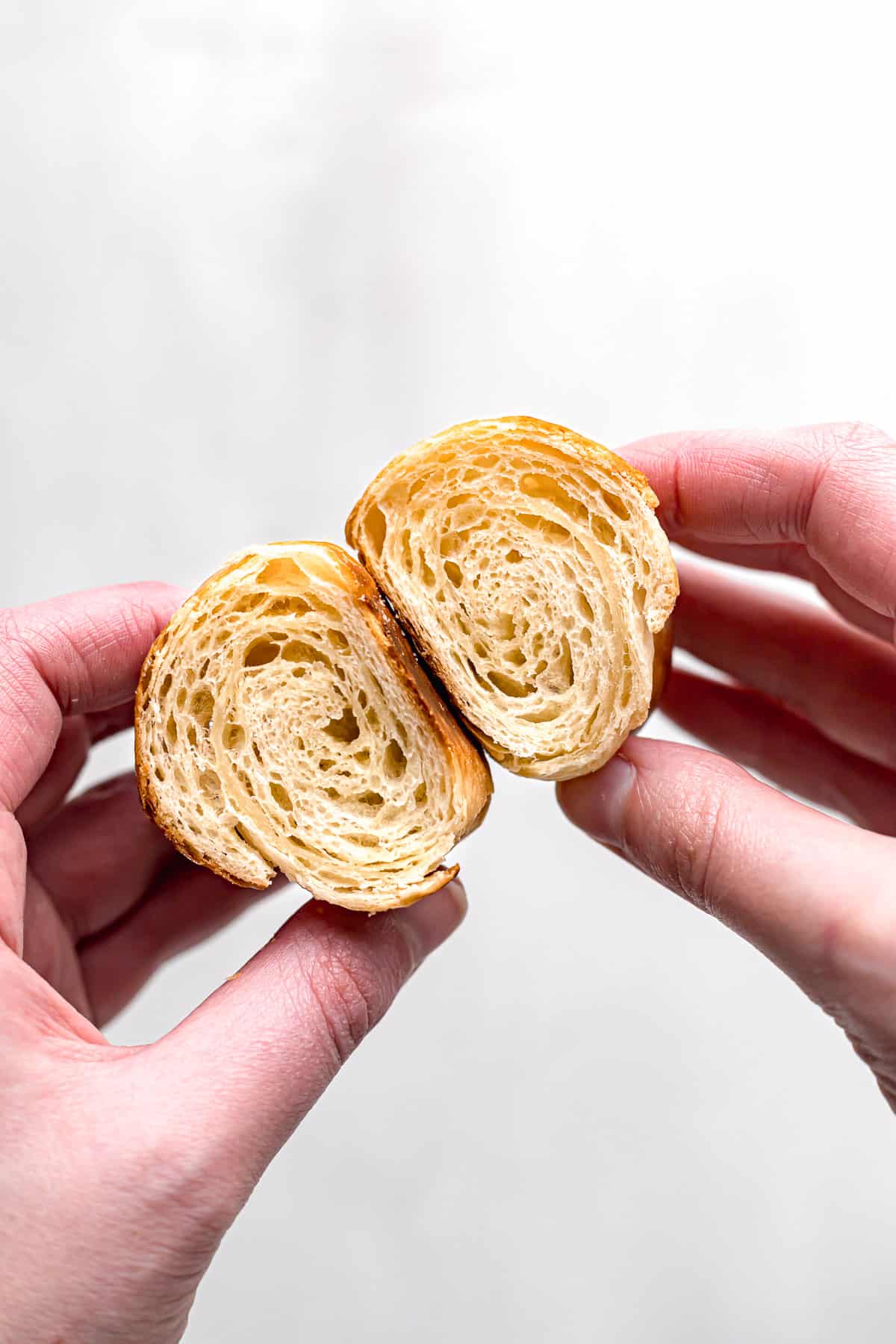 mini croissant cut in half to show inside texture held in two hands.