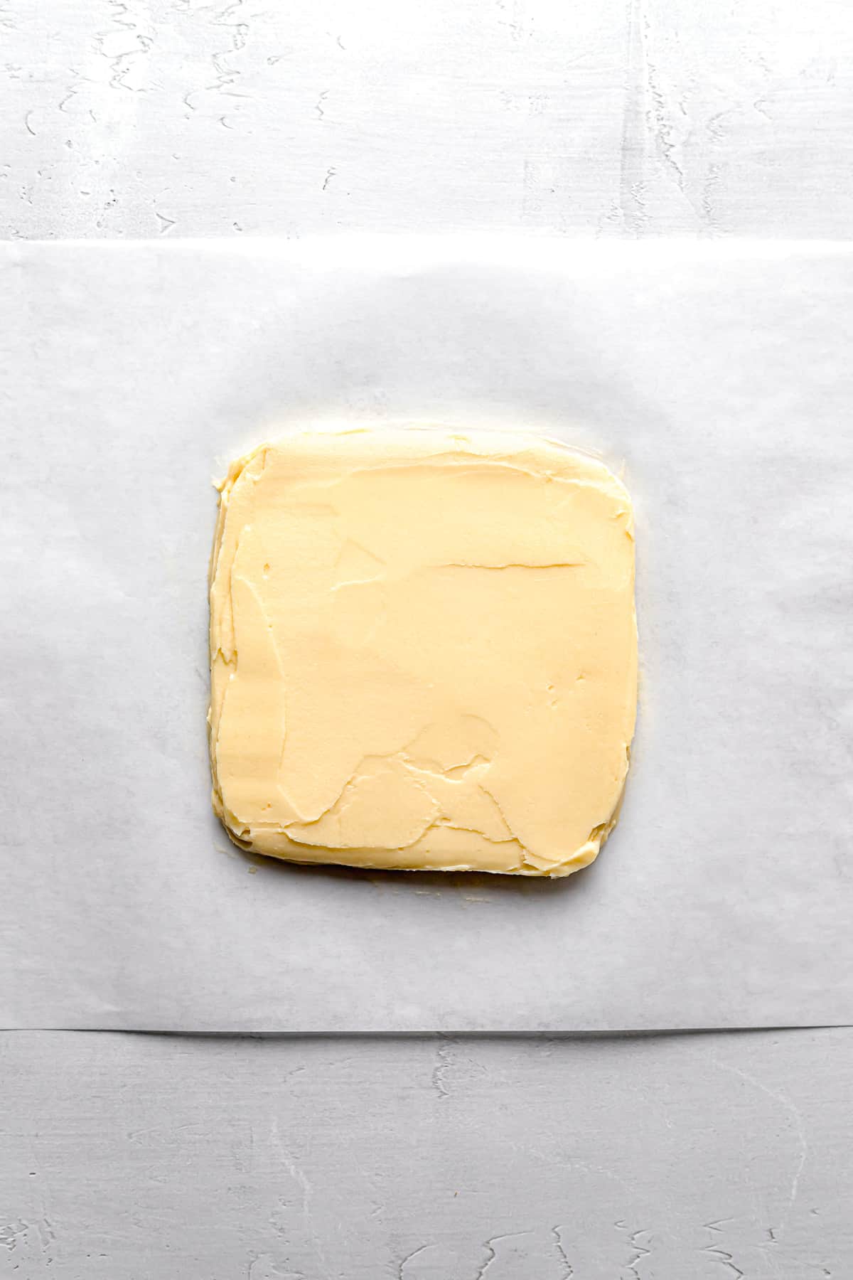 butter block shaped into square on parchment paper.