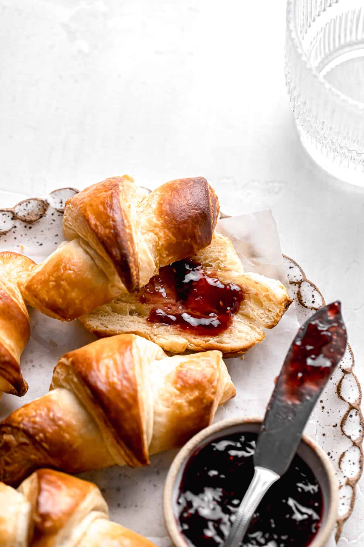 small batch mini croissants on plate with one cut in half and jam spread on top.