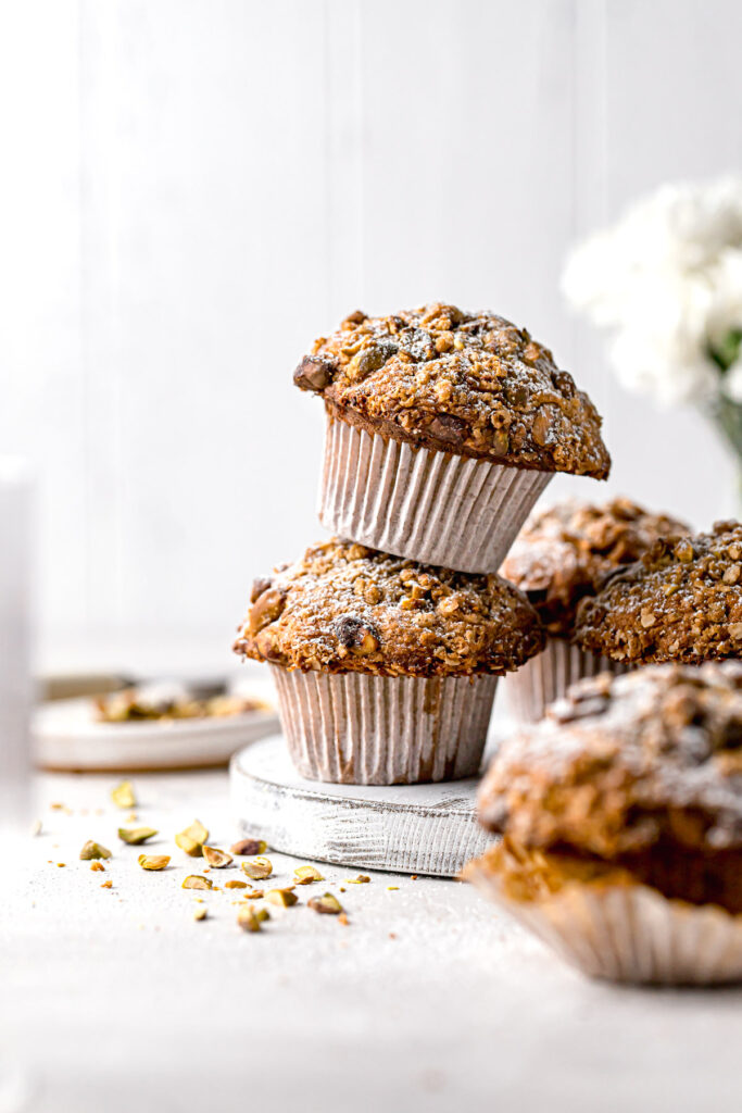 two pistachio muffins with oat streusel topping stacked on white board