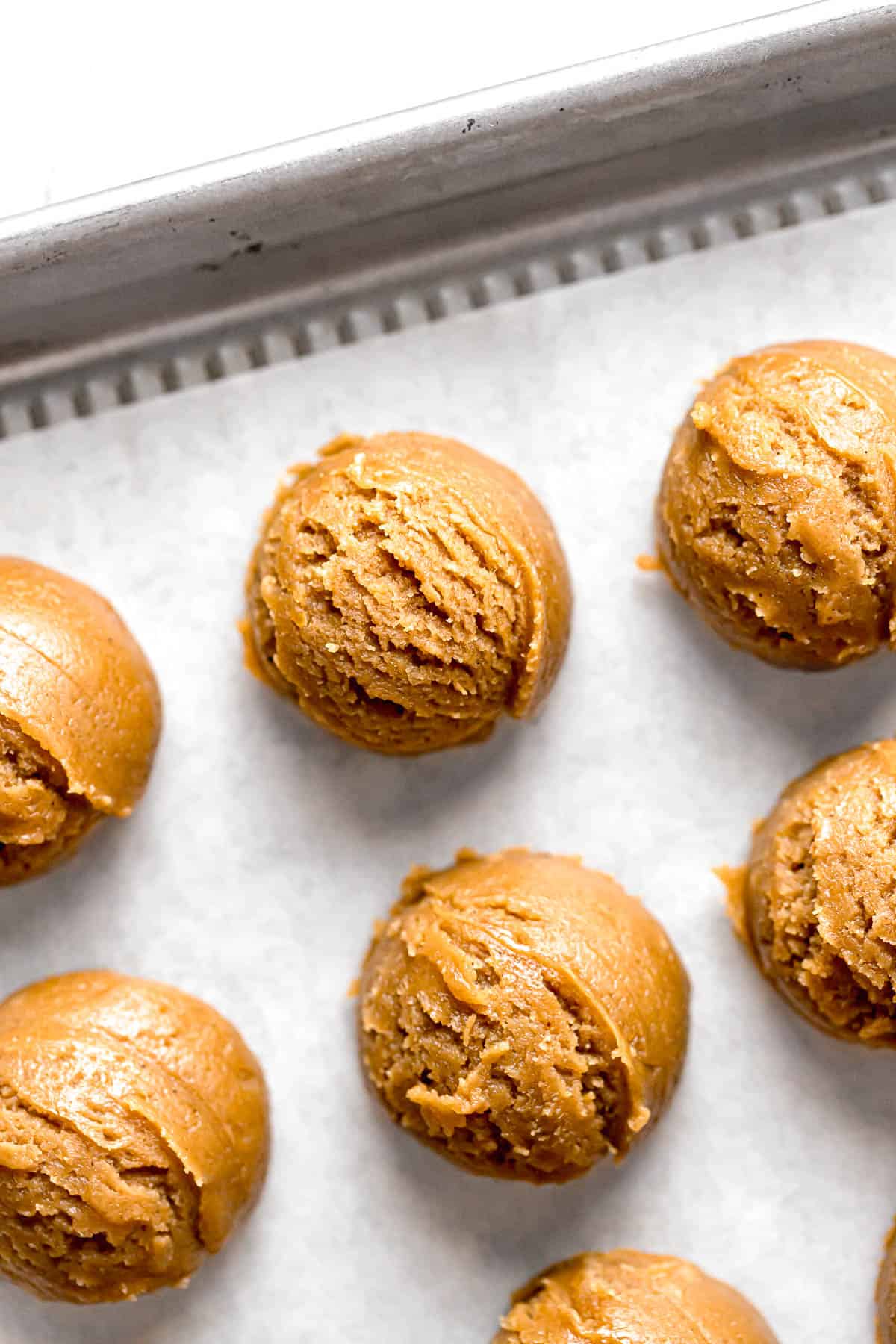 peanut butter cookie dough balls on parchment lined baking sheet.