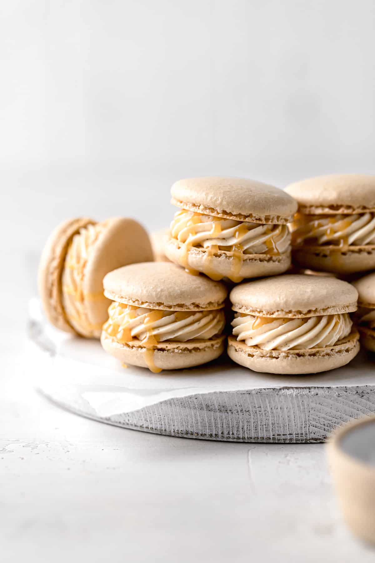 salted caramel macarons piled on white wooden board.
