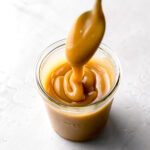 salted caramel sauce in glass jar with caramel drizzling off of spoon
