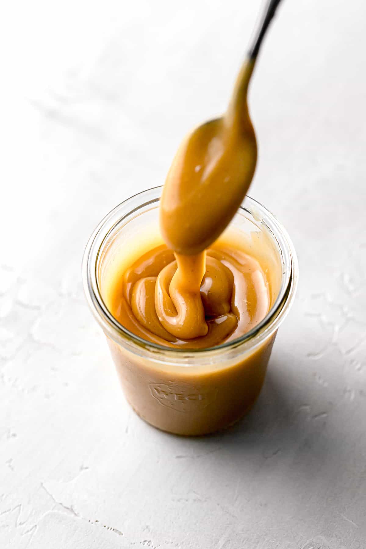 salted caramel sauce in glass jar with caramel drizzling off of spoon.