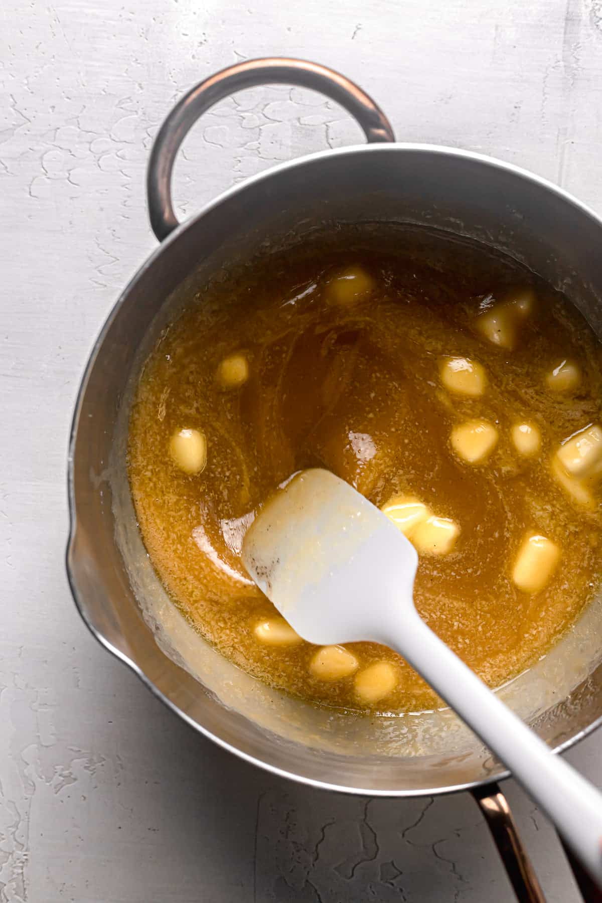 butter and vanilla being stirred into caramel sauce.