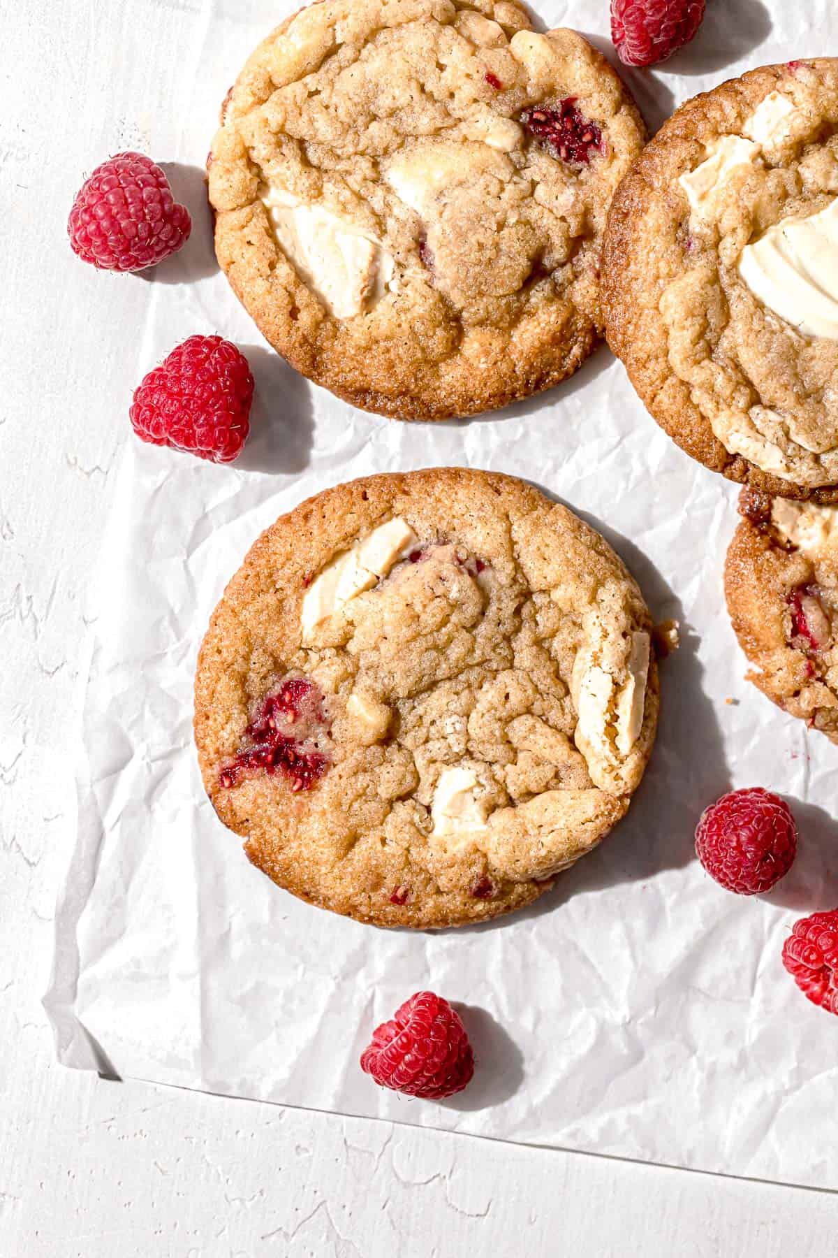 raspberry white chocolate cookies on parchment paper with fresh raspberries.