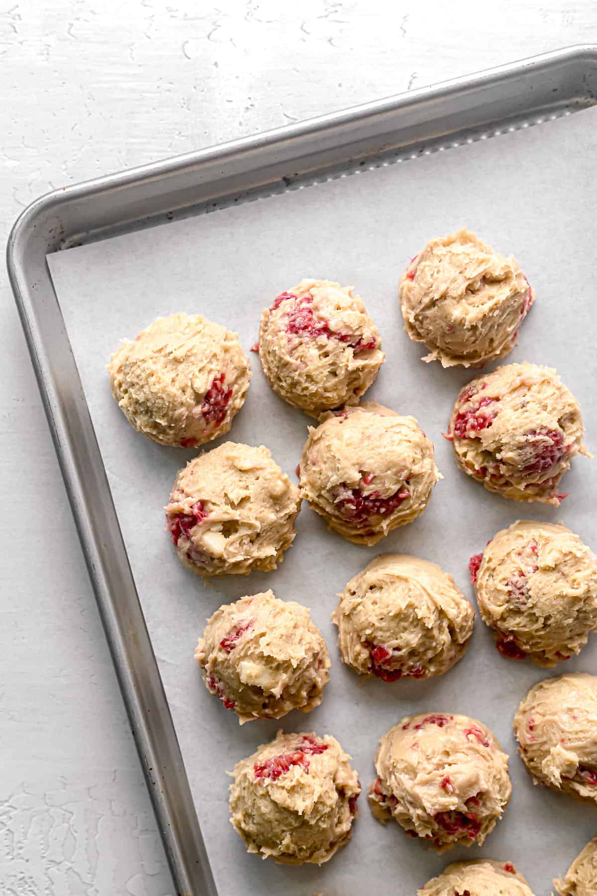 cookie dough balls lined up close together on parchment lined baking sheet
