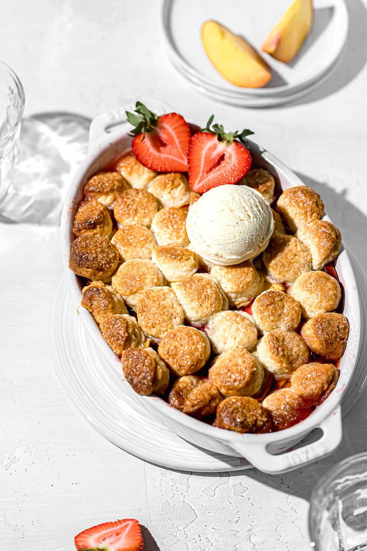 strawberry peach cobbler with cream biscuits in oval dish.