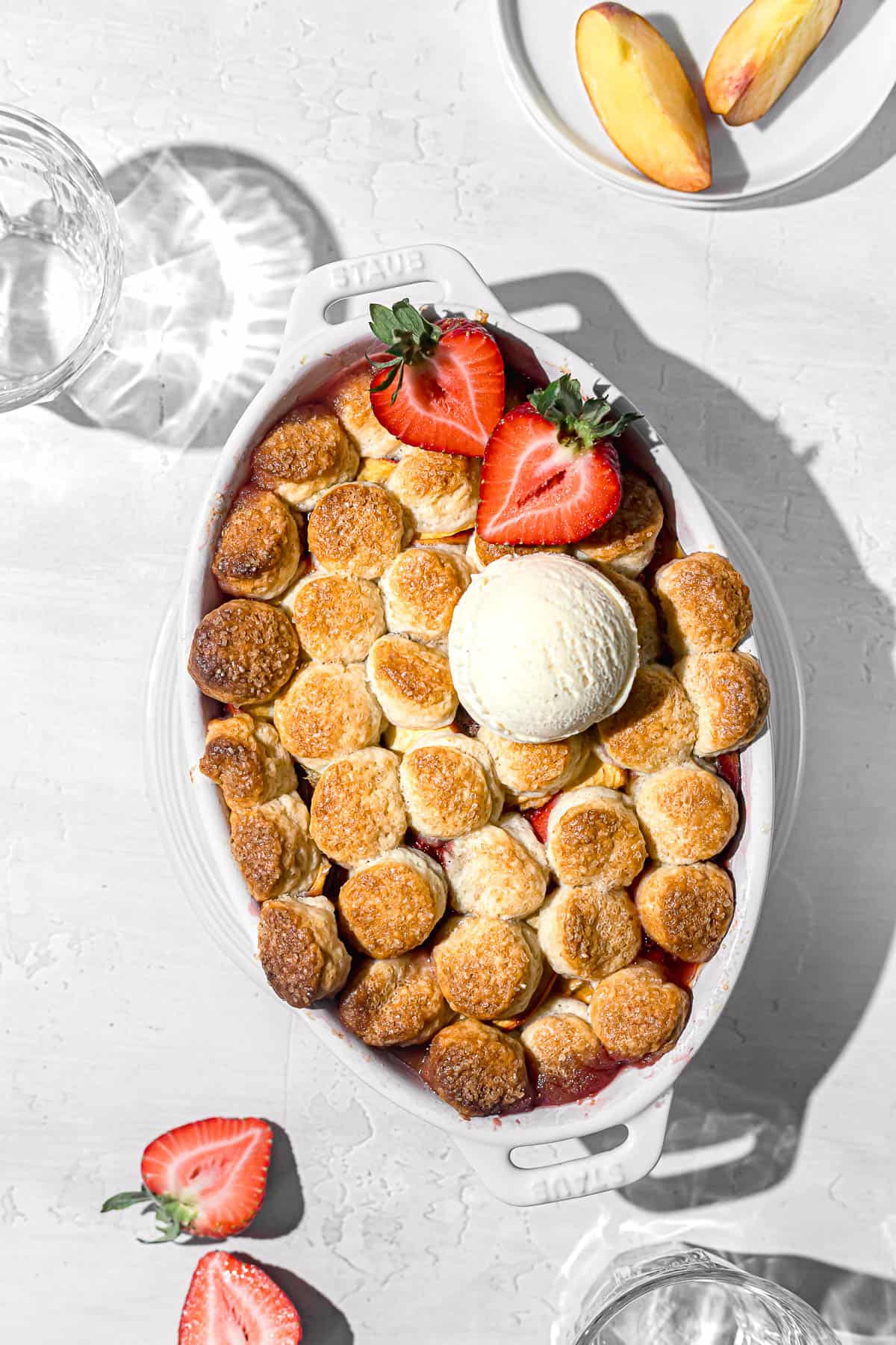 baked strawberry peach cobbler in oval dish topped with ice cream