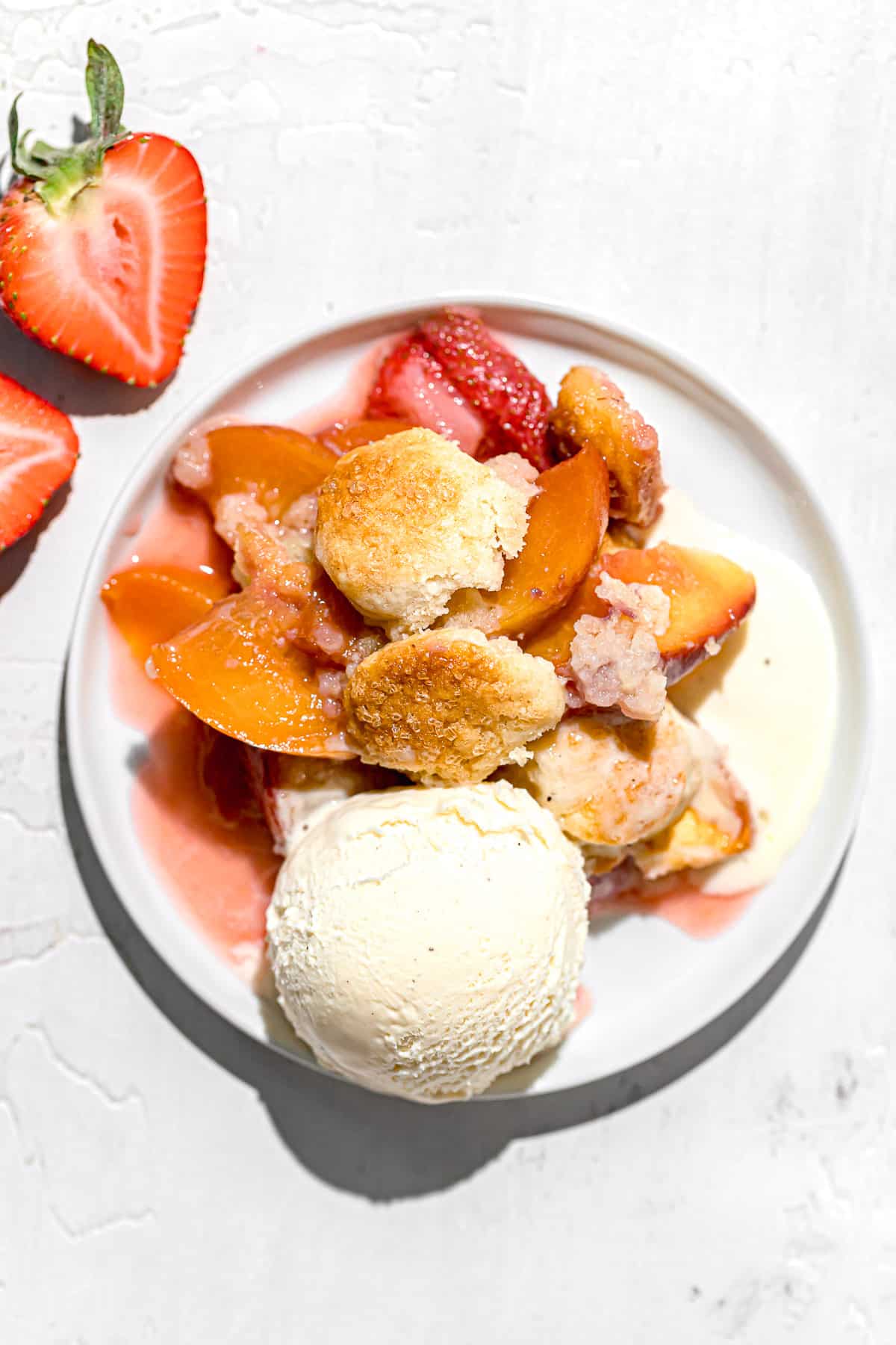 strawberry peach cobbler spooned onto plate with scoop of vanilla ice cream.